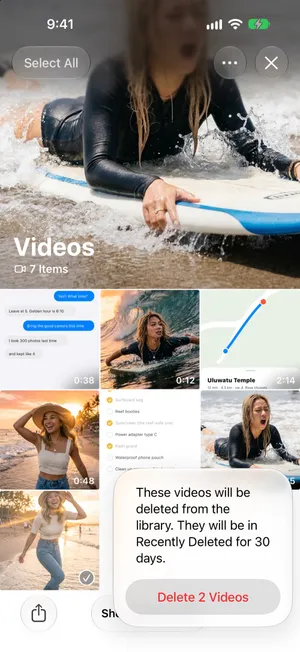 La raccolta Video in modalità di selezione con due clip lunghe spuntate, e la conferma di Foto in inglese: «These videos will be deleted from the library. They will be in Recently Deleted for 30 days.» con il pulsante «Delete 2 Videos»